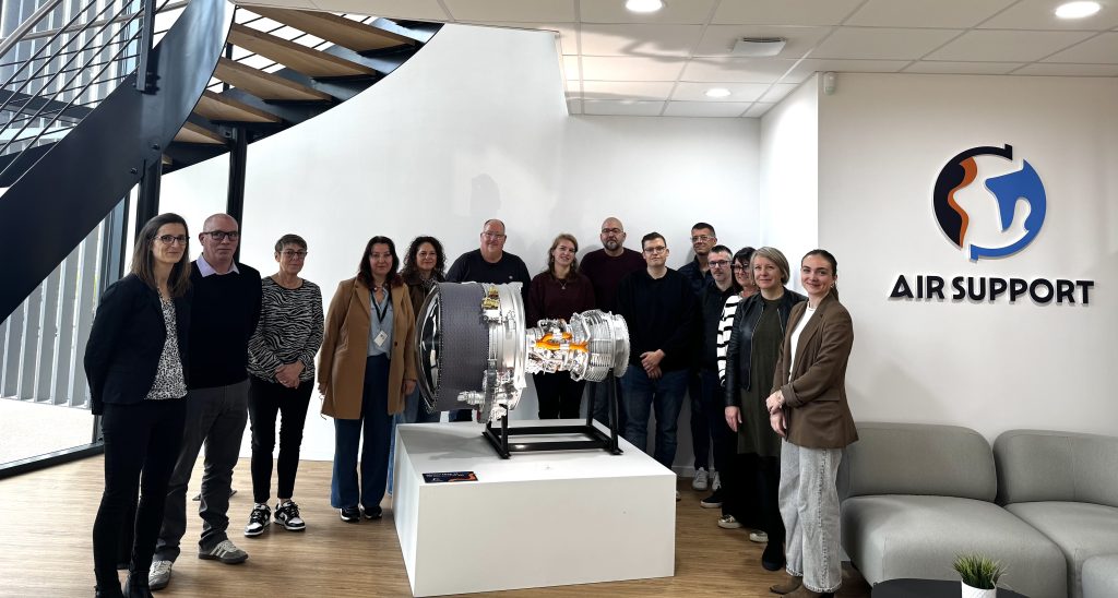 Groupe de salariés de l'entreprise Air Support réunis autour d'une maquette de moteur d'avion dans le hall d'accueil de l'entreprise lors de la Semaine de l'Industrie.